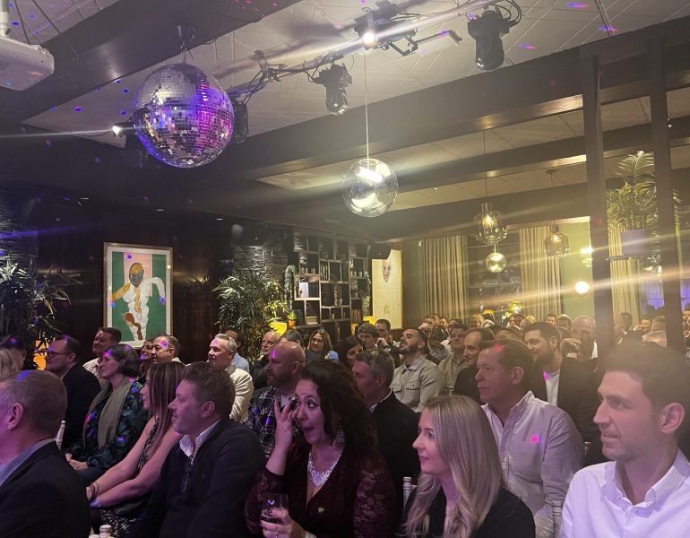 A crowd sit facing forward and are laughing